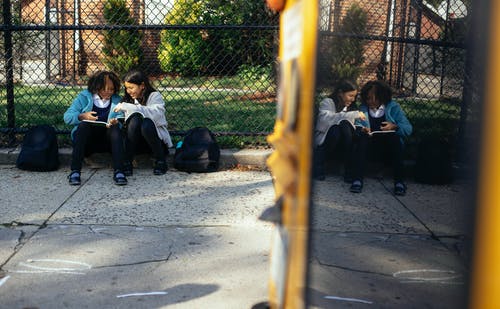 性格开朗的多民族女学生坐在学校围栏附近的教科书 · 免费素材图片