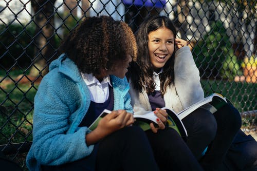 坐在公园的教科书的快乐的多种族女小学生 · 免费素材图片