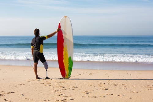 不可识别的截肢男子冲浪者与冲浪板站在海边 · 免费素材图片