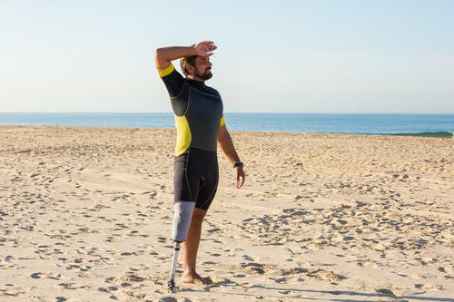 运动员截肢者站在沙滩上时擦汗 · 免费素材图片