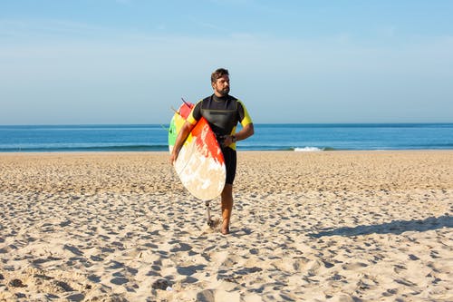 残疾人携带冲浪板在沙滩上 · 免费素材图片