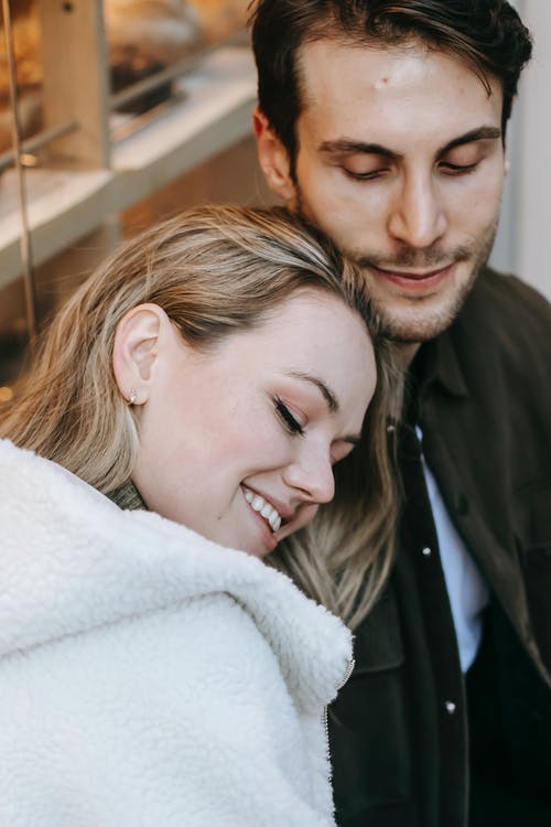 白色皮大衣在黑色夹克的男人旁边微笑的女人 · 免费素材图片