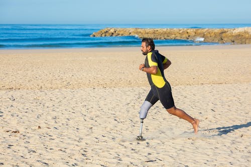 坚定的运动员，腿假肢在沙质海岸线上运行 · 免费素材图片