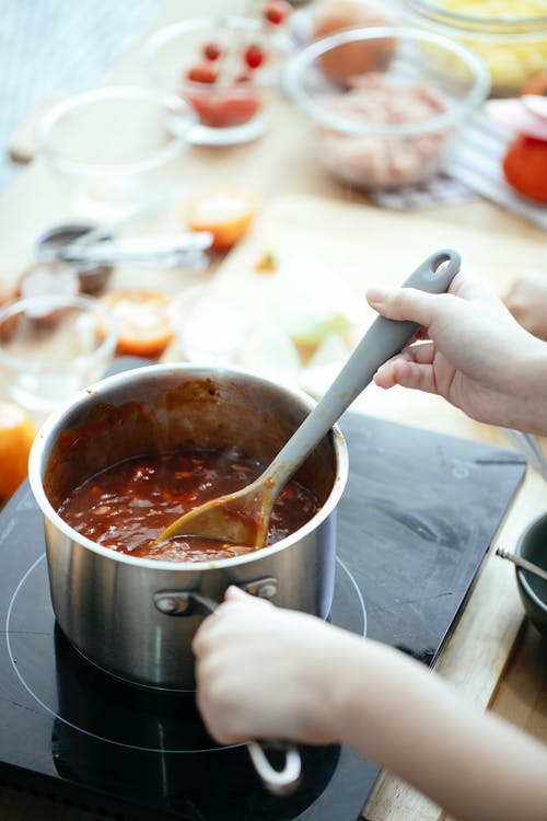 拿着银钢烹饪锅用棕色液体的人 · 免费素材图片