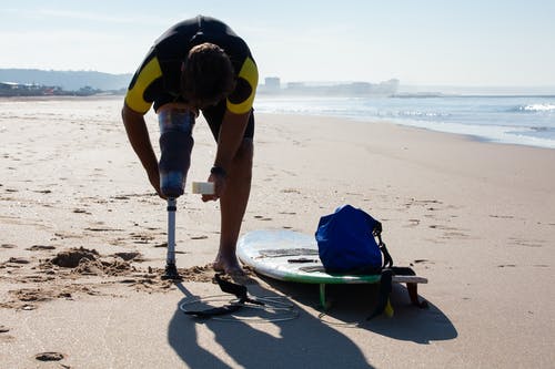 不可识别的男性冲浪截肢者用胶带在海滩上包裹假体 · 免费素材图片