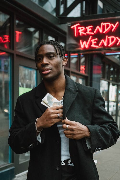自信的年轻黑人男性站在大街上，把折叠的报纸放在外套的口袋里 · 免费素材图片