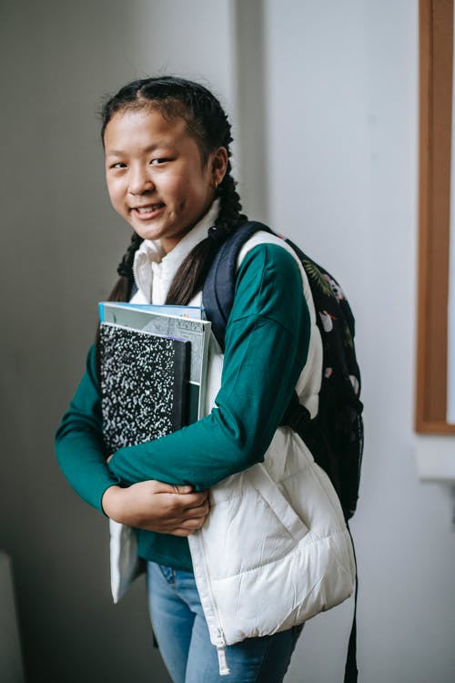 快乐的民族女学生与学习后站在教室里的堆栈的教科书 · 免费素材图片