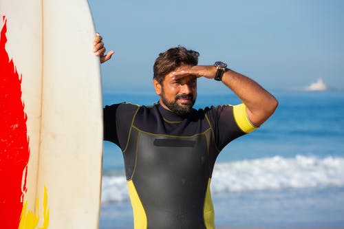 满足种族男性冲浪者站在海边的冲浪板附近 · 免费素材图片