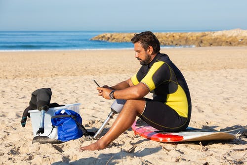 在海滩上使用智能手机的腿部假肢聚焦民族运动员 · 免费素材图片