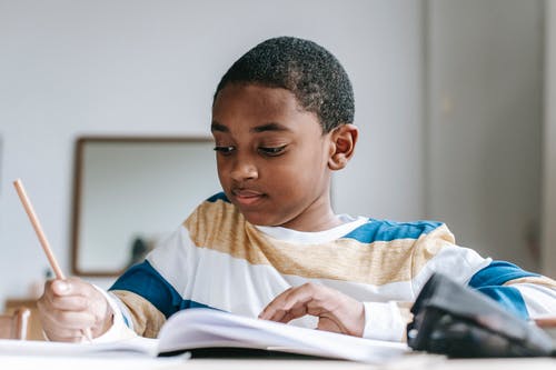 做在习字簿的正面黑人男孩家庭作业 · 免费素材图片