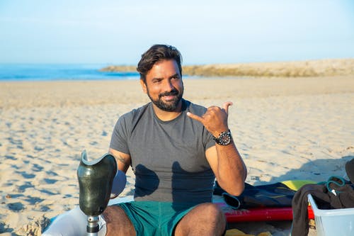 晒黑的残疾的男子显示沙加坐在海滩上 · 免费素材图片