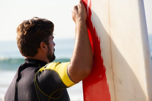 大胡子的男性冲浪者，站在海边的冲浪板 · 免费素材图片