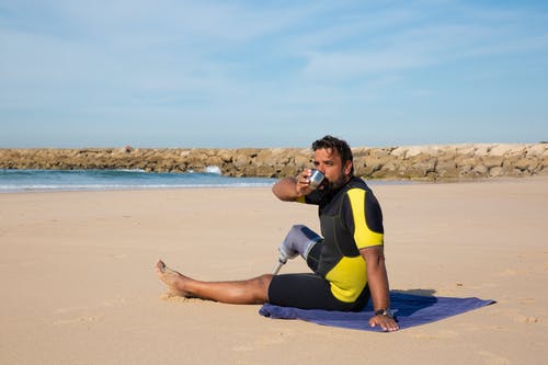 在海边休息，从热水瓶里喝酒的族裔男性截肢者 · 免费素材图片