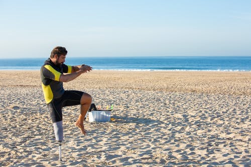 运动的人截肢者在海岸上热身时举起双腿 · 免费素材图片