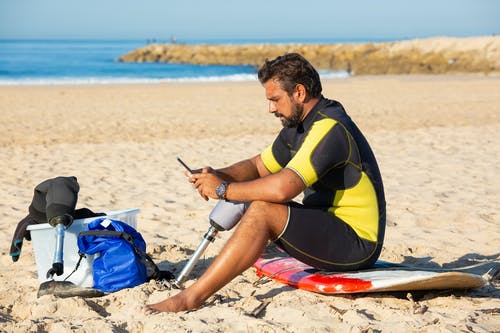 假肢在海滩上使用智能手机的人 · 免费素材图片