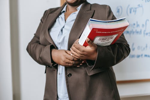 有书的匿名黑人女性家庭教师在学校附近站立在白板 · 免费素材图片