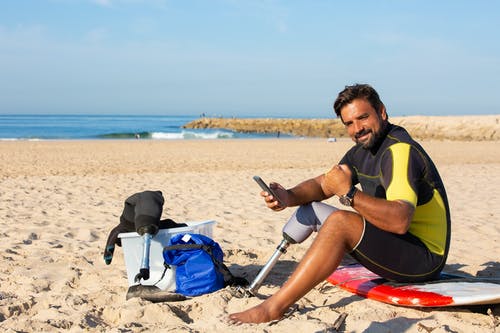 在海滩上使用智能手机的满足种族截肢男性冲浪者 · 免费素材图片