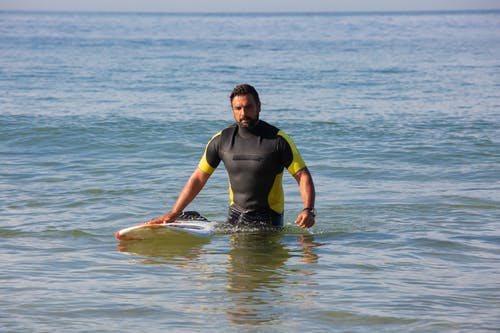 集中民族男性冲浪者站在海水中的冲浪板 · 免费素材图片