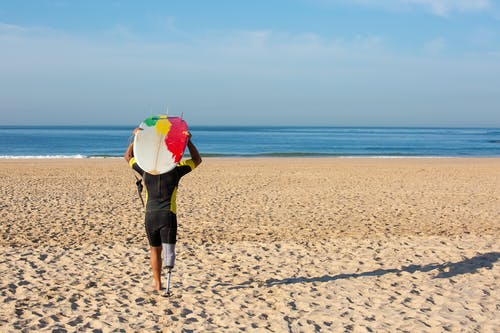 不可识别的截肢男性冲浪者携带冲浪板头朝大海 · 免费素材图片