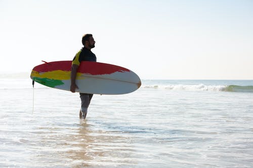 男性截肢者冲浪者与冲浪板站在海水中 · 免费素材图片
