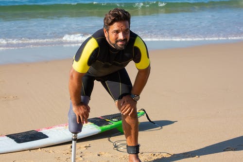 男性的截肢者冲浪者站在一起在海滩上的膝盖上的手 · 免费素材图片