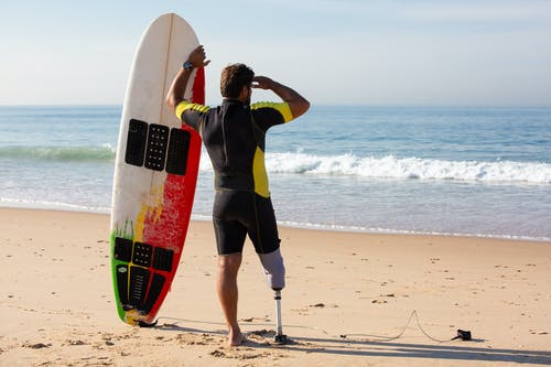 无法识别男性截肢者冲浪者站在海边的冲浪板 · 免费素材图片