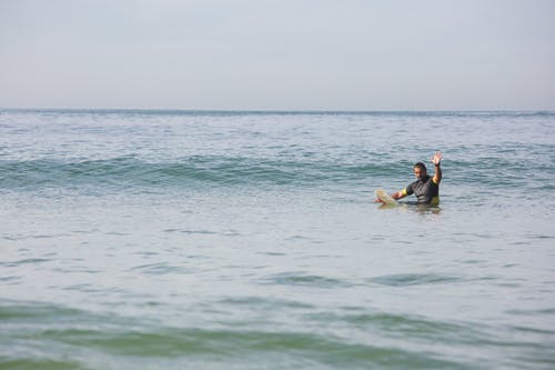 运动的男性冲浪者，站在海水中，挥舞着的手 · 免费素材图片