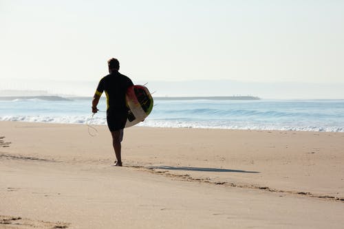 男性冲浪者携带冲浪板在沙滩上的剪影 · 免费素材图片