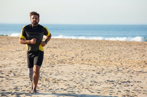 专用的民族运动员截肢者在沙质海岸线上慢跑 · 免费素材图片