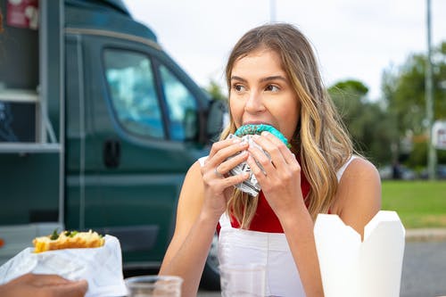 年轻女子在街边咖啡馆吃汉堡 · 免费素材图片