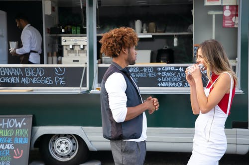 年轻多样的夫妇站在外卖卡车附近吃外卖三明治 · 免费素材图片