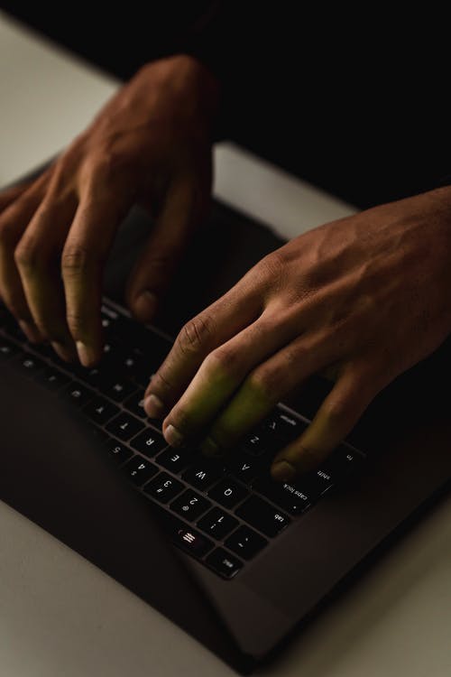 作物在黑暗中在笔记本电脑键盘上打字的不露面的人 · 免费素材图片