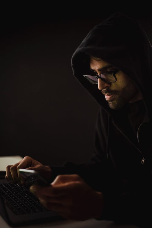 集中的黑客在黑暗中浏览笔记本电脑和智能手机 · 免费素材图片