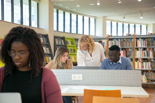 在女老师的协助下在图书馆的笔记本电脑上接班的年轻不同学生 · 免费素材图片