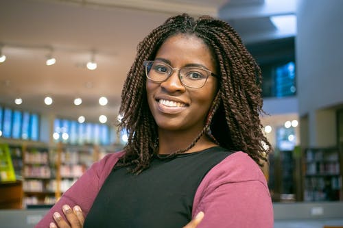 微笑着扎着辫子的黑人妇女在图书馆 · 免费素材图片