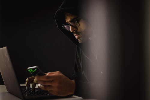 在黑暗中在笔记本电脑上打字的智能手机作物族黑客 · 免费素材图片