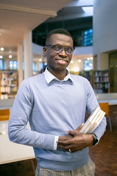 有书的微笑的黑人男学生在图书馆里 · 免费素材图片