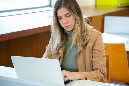 膝上型计算机的严肃的妇女在图书馆里 · 免费素材图片