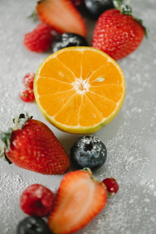 一半的新鲜草莓和橙与蓝莓在冰上 · 免费素材图片