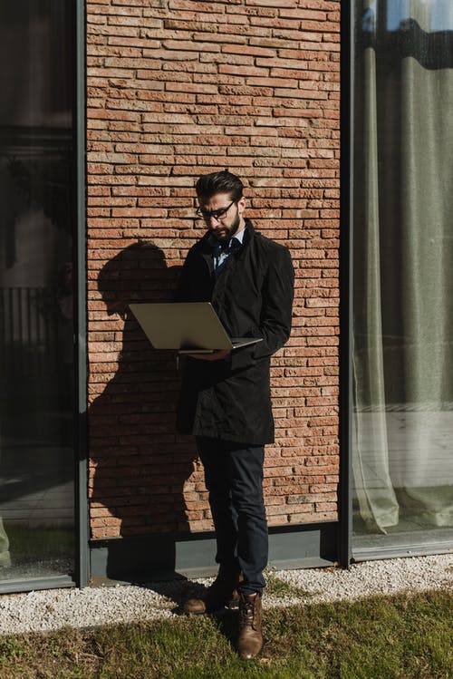 蓝色夹克和黑色的裤子，站在棕色砖墙旁边的人 · 免费素材图片