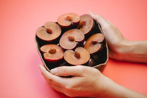 收获女性服务碗的开胃对半李子粉红色的桌子上 · 免费素材图片