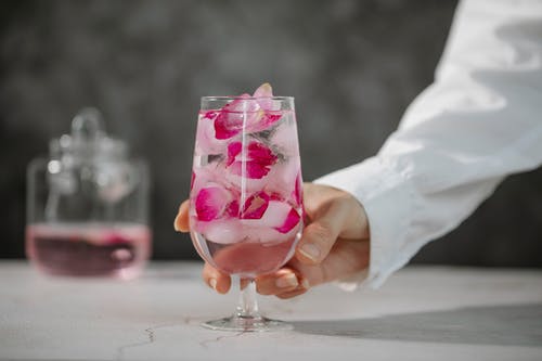 持有透明酒杯与粉红色液体的人 · 免费素材图片