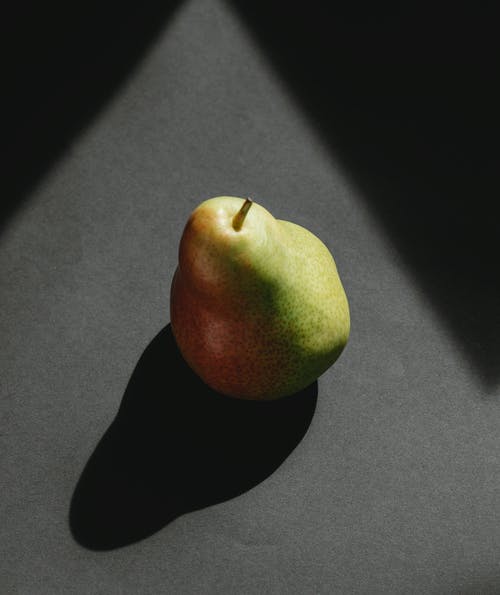 成熟的整个梨在灰色的表面上投射阴影 · 免费素材图片