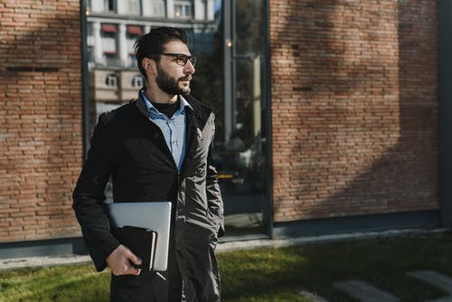 拿着黑色便携式计算机的黑色皮夹克的男人 · 免费素材图片