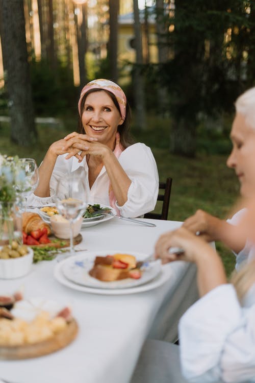 白色背心的女人坐在桌子前的椅子上的食物 · 免费素材图片