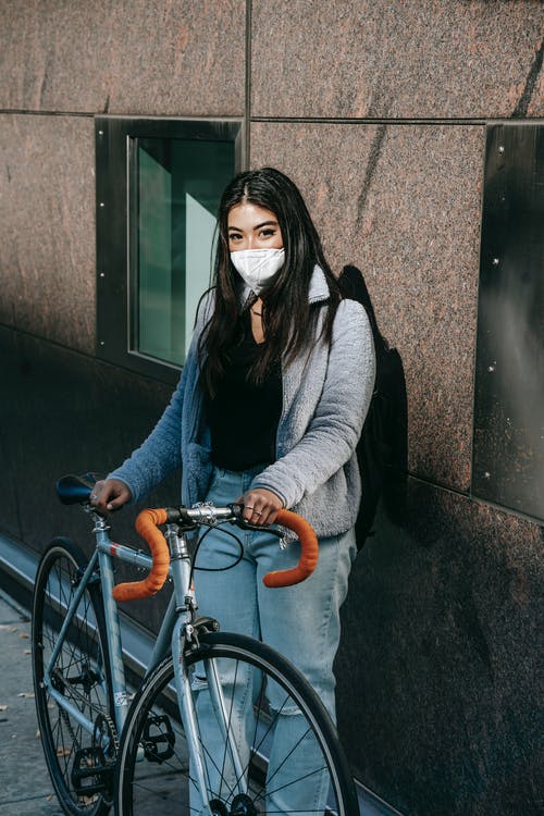 灰色外套和黑色围巾站在橙色自行车旁边的女人 · 免费素材图片