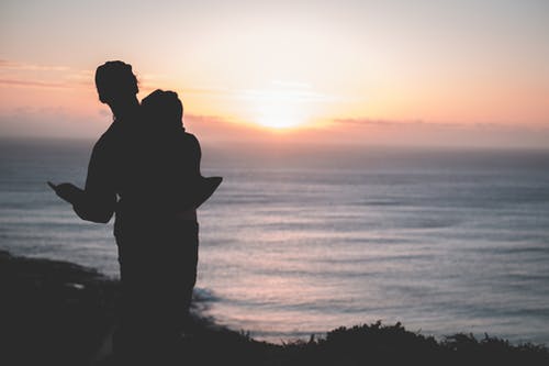 情侣站在海边日落时的剪影 · 免费素材图片