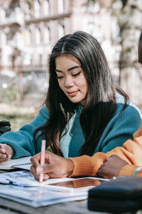 蓝色和橙色毛衣握笔的女人 · 免费素材图片