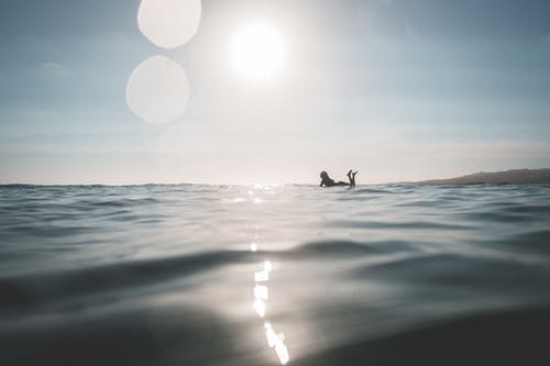 在阳光下的海在冲浪板上游泳的女人 · 免费素材图片
