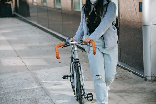 站在黑色自行车旁边的灰色外套和蓝色牛仔牛仔裤的女人 · 免费素材图片